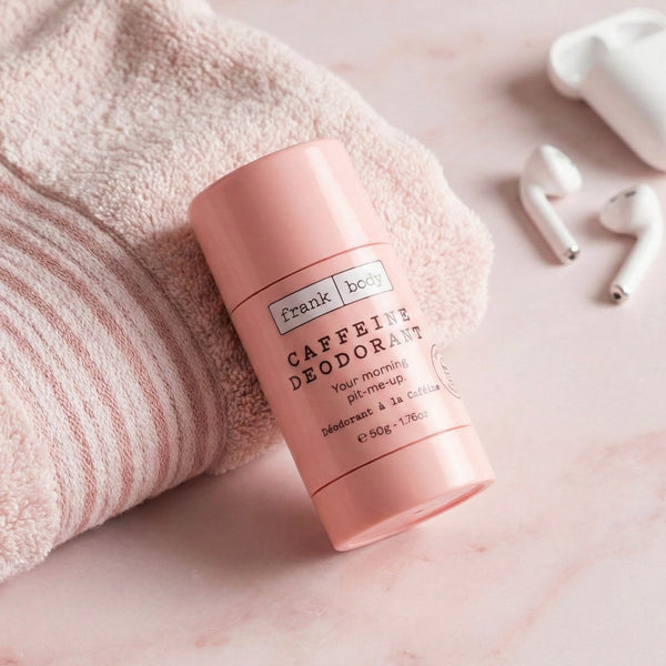A pink stick of frank body Caffeine Deodorant resting on a folded pink towel beside earphones.