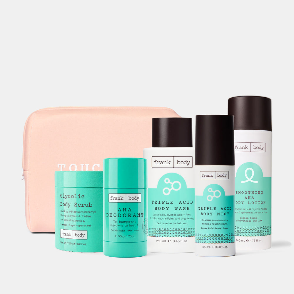 A set of Frank Body body care products and a zippered pouch on a light gray background. The set includes a glycolic body scrub, an aha deodorant, a triple acid body wash, a triple acid body mist, a brooding ara body lotion, and a pale pink zippered pouch.