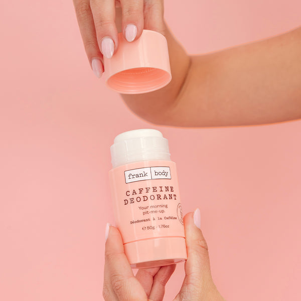 Hands opening a pink frank body Caffeine Deodorant stick on a pink background.